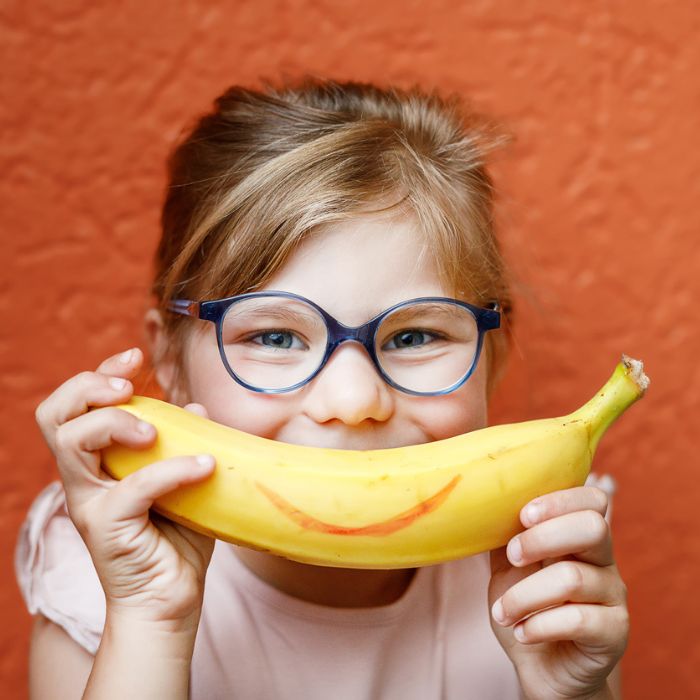 Little girl smiling and holding up a banana
