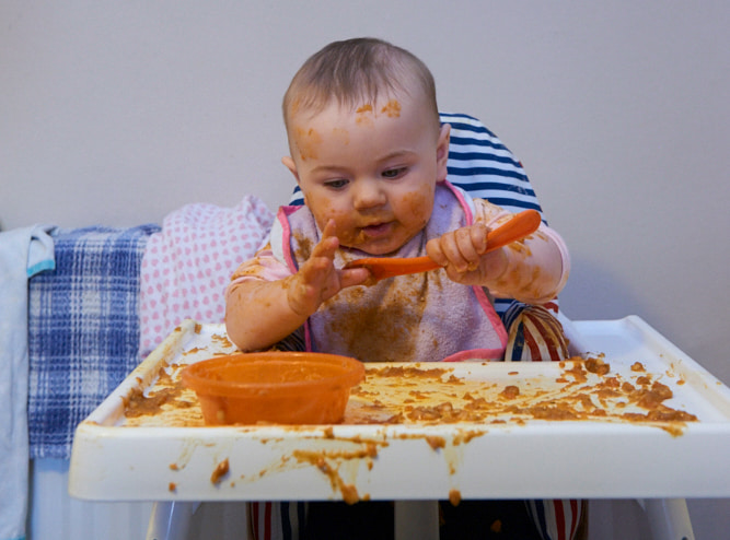 Photo of a messy baby holding a spoon 