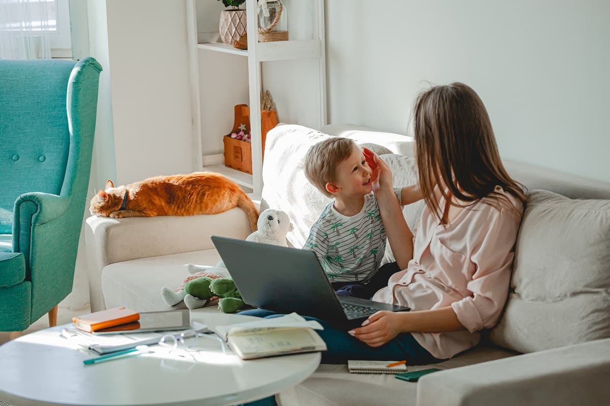 Mother and toddler on sofa with cat, a laptop open in front of them