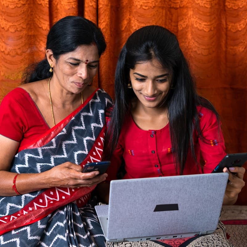 Mother and daughter looking at their phones and a laptop