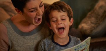 Image of a child and mum looking at a book together and laughing.