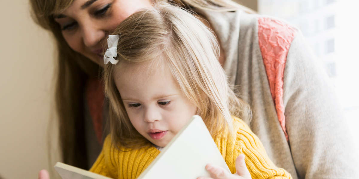 Image of a child sitting on their mum's lap, looking at a book together.