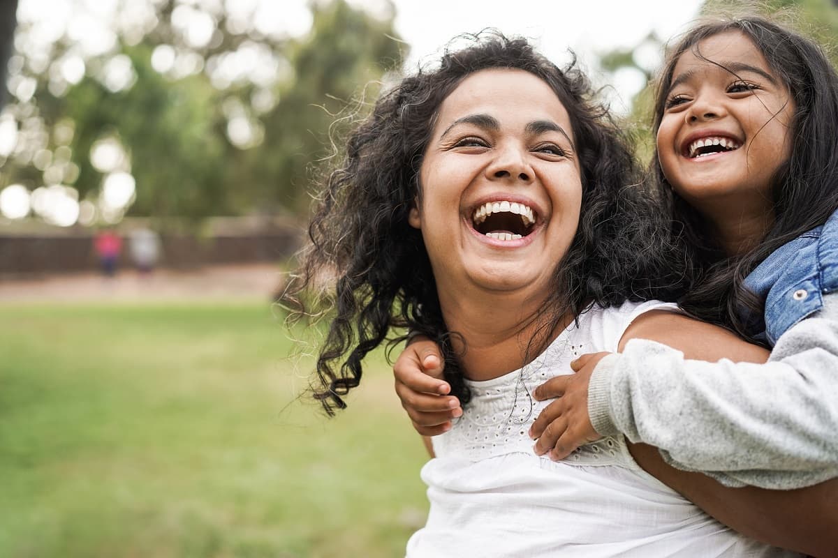 Mum and daughter outside in a park, both smiling and laughing