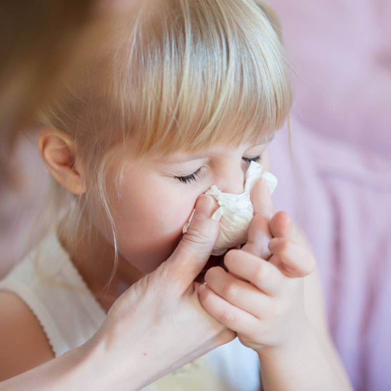 Image of a mum holding a tissue to a child's nose.