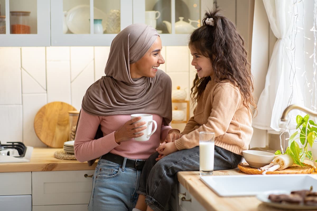 Mum wearing hijab and girl in the kitchen, talking