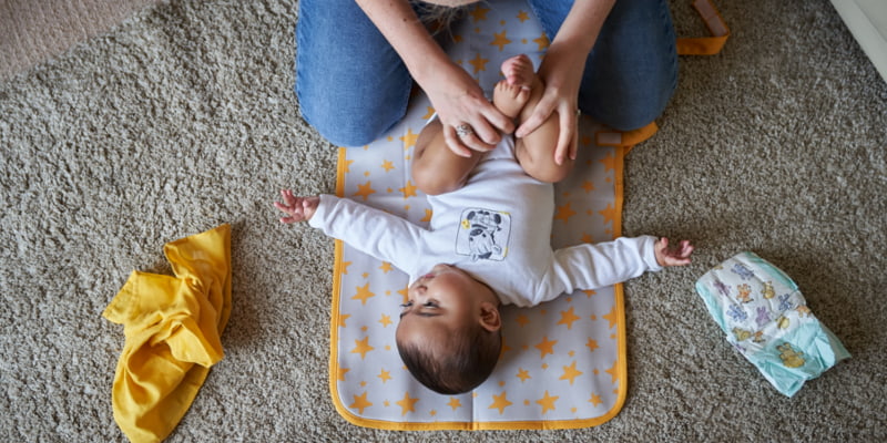 Image of a baby lying on a mat, with their mum sitting next to them holding their feet.