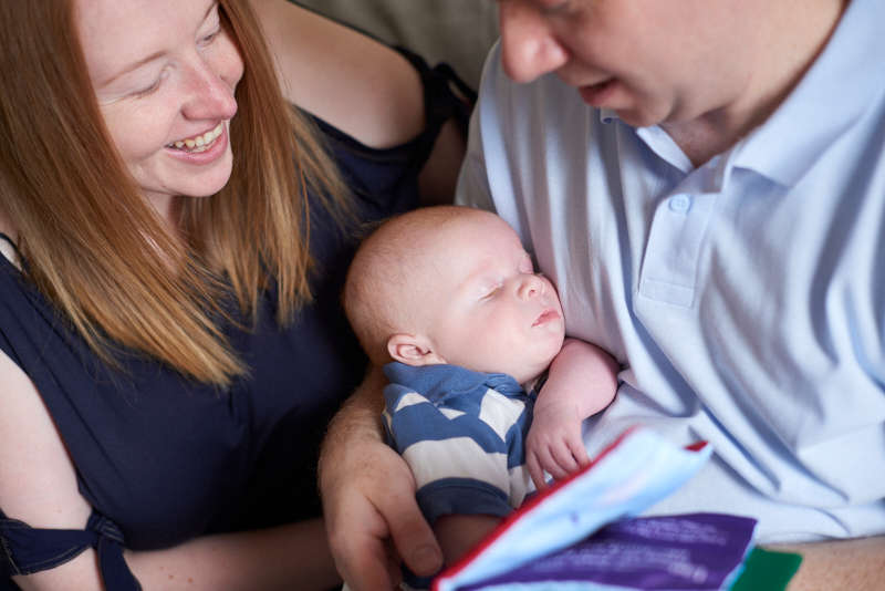 Image of a mum and dad smiling at a sleeping baby in the dad's arms.