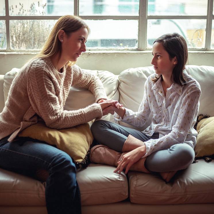 Mother and teen daughter sitting on a sofa talking together