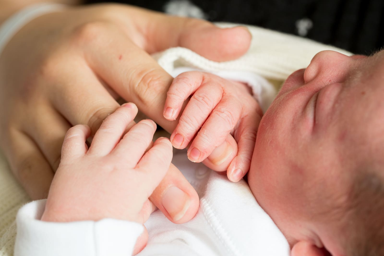 Image of a newborn baby holding an adult's hand.