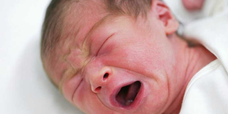 Photo of a newborn baby crying in bed