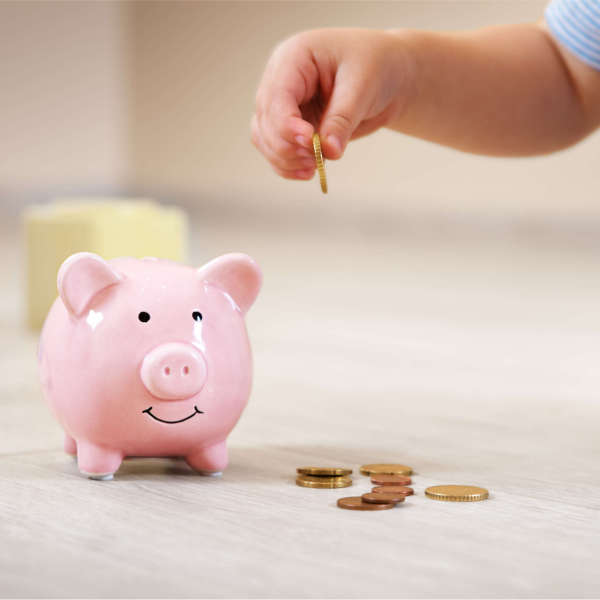 Image of a child's hand putting a coin in a pink piggy bank.