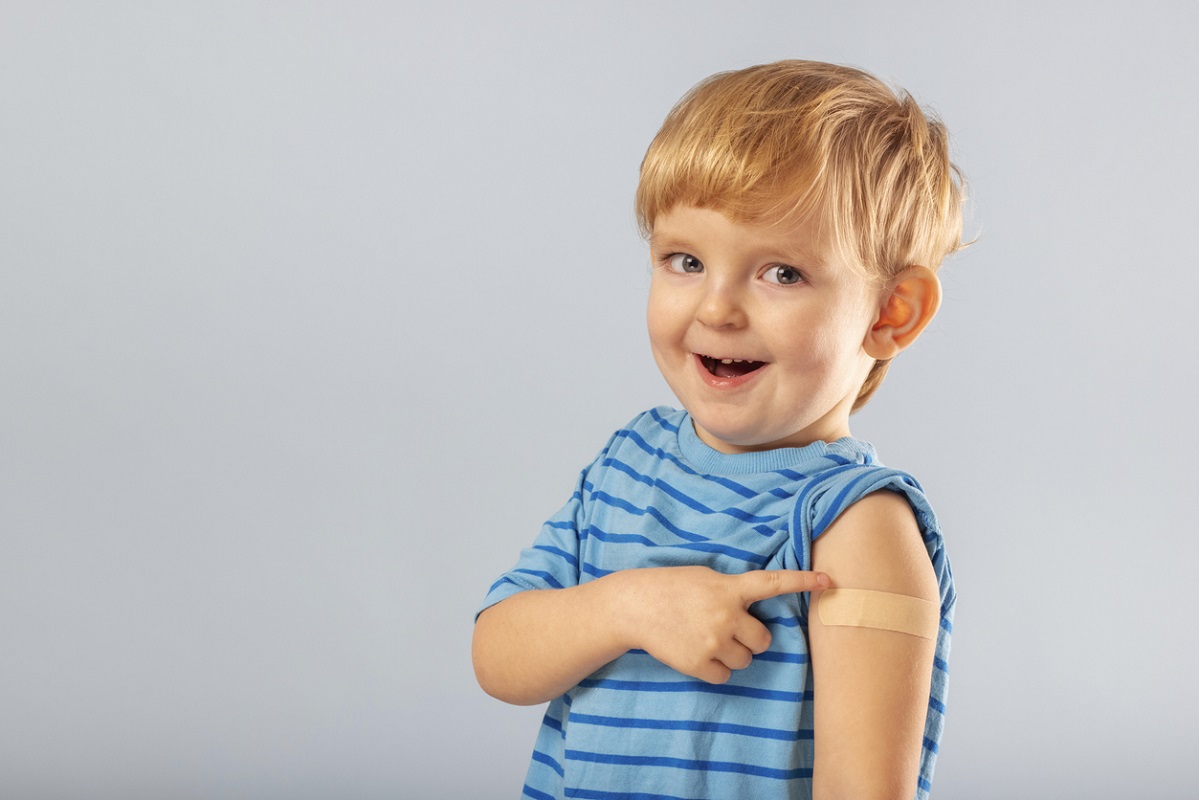 Little boy smiling and pointing to a vaccination plaster on his arm
