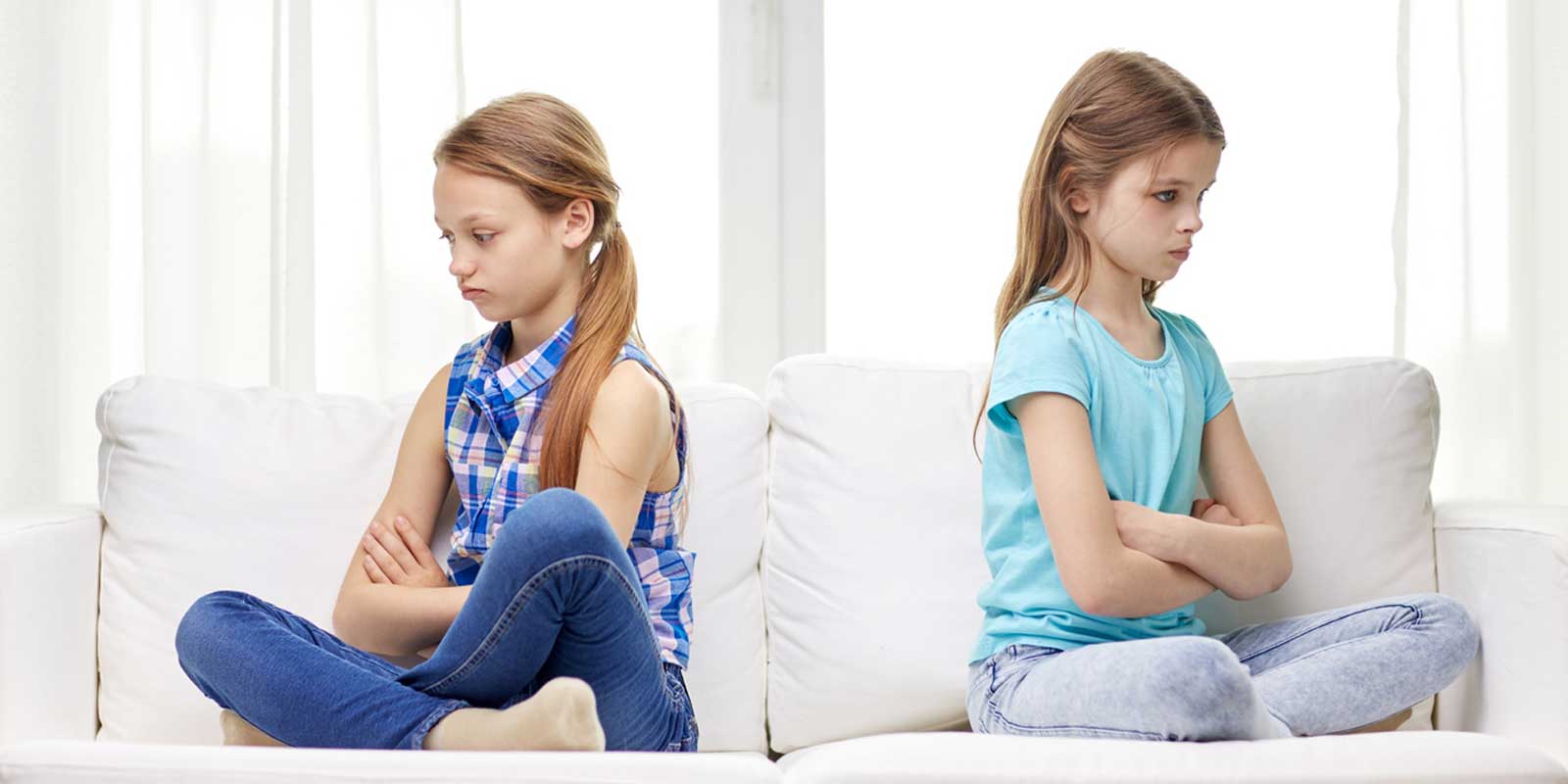 Two girls sitting back to back with their arms folded, looking cross