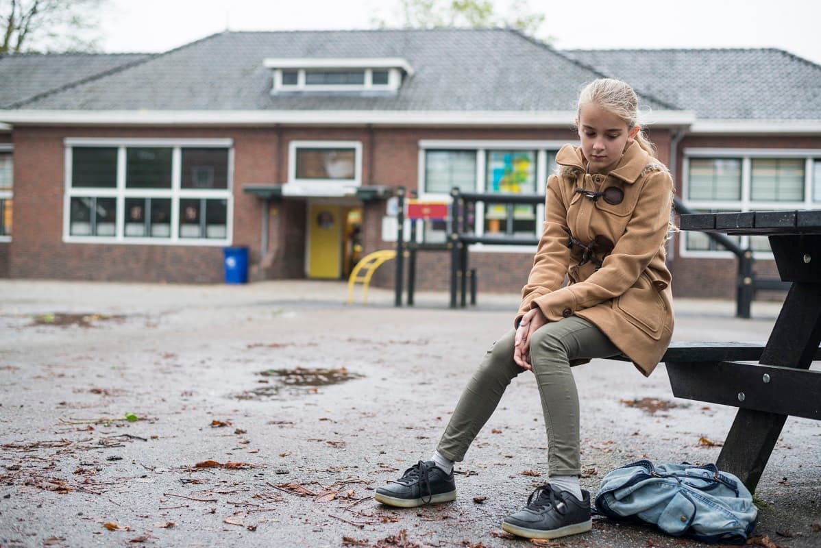 Sad girl sitting on a bench in a school playground