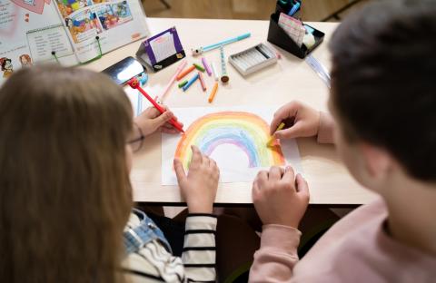 Young child and parent drawing a rainbow together