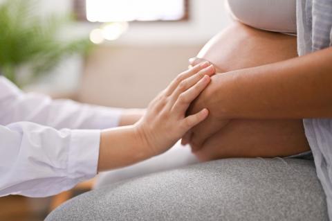 Woman's hands holding the hands of a pregnant woman over her belly