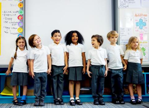 Primary school children standing in front of a whiteboard in a classroom.