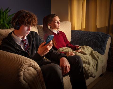 Boy and girl sitting on a sofa, the boy looking at his phone.
