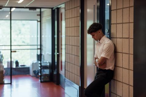 Boy standing alone in a school corridor looking sad.