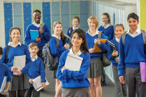Group of school pupils wearing uniform, holding folders, standing in corridor.