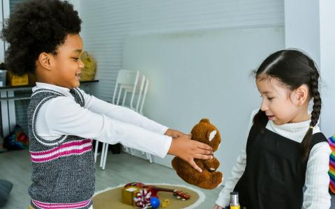 Young boy offering a girl a teddy bear to play with.