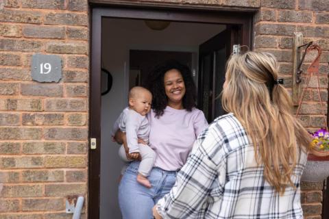 Mother and baby greeting their health visitor at the door.