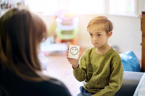 Small boy holding up a card with a smiley face on it.
