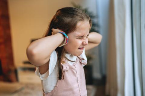 Young girl with her hands over her ears and her eyes squeezed shut.