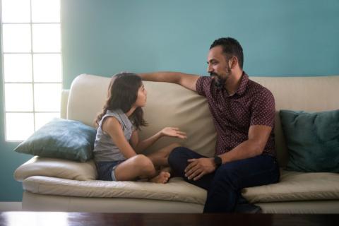 Father and daughter sitting on a sofa, chatting.