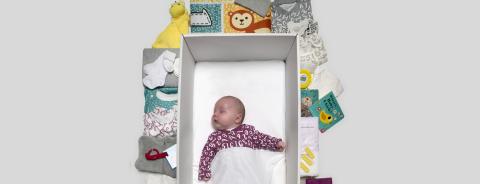 Baby asleep in the Baby Box surrounded by items from the box