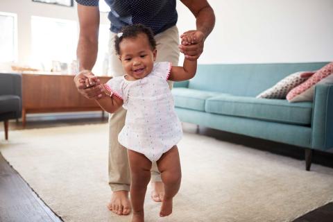 Photo of a baby being helped to walk by dad