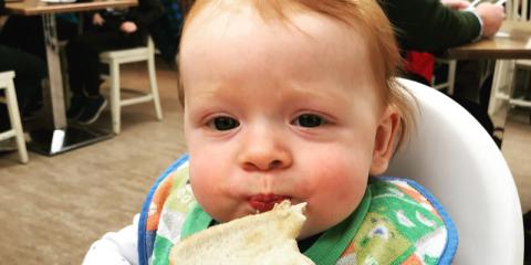 baby in a high chair eating a sandwich