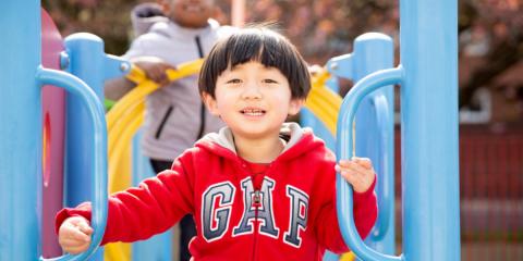 Image of a child smiling at the camera while playing on a climbing frame in a play park.