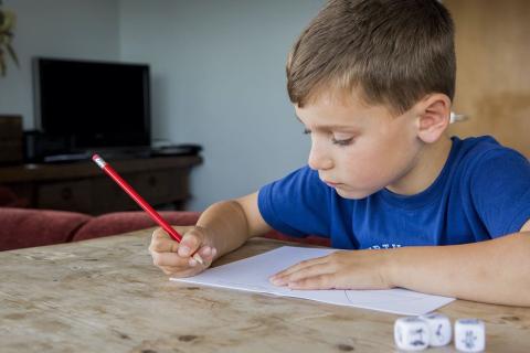 Image of a child sitting at a table writing with a pencil.
