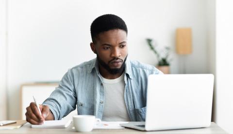 Man looking at laptop and making notes