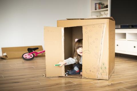 Toddler girl playing inside a big cardboard box
