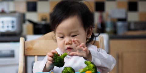 toddler in chair picking at some broccoli 
