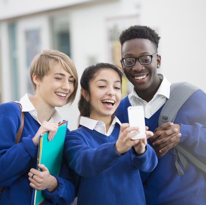 Three smiling teens wearing school uniform taking a selfie with a phone