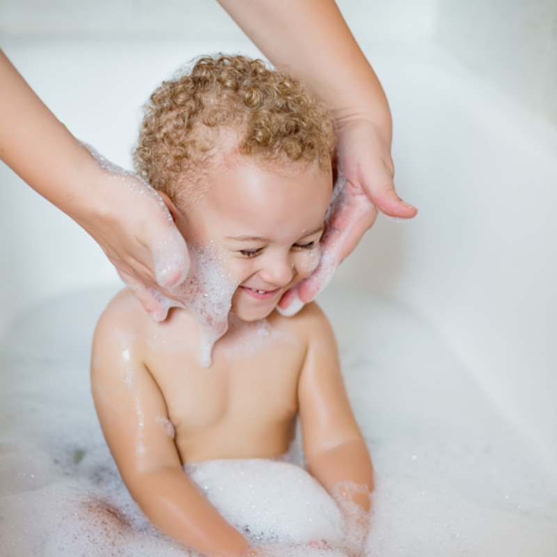 Image of a mum washing a laughing toddler's face while the toddler sits in a bubble bath.
