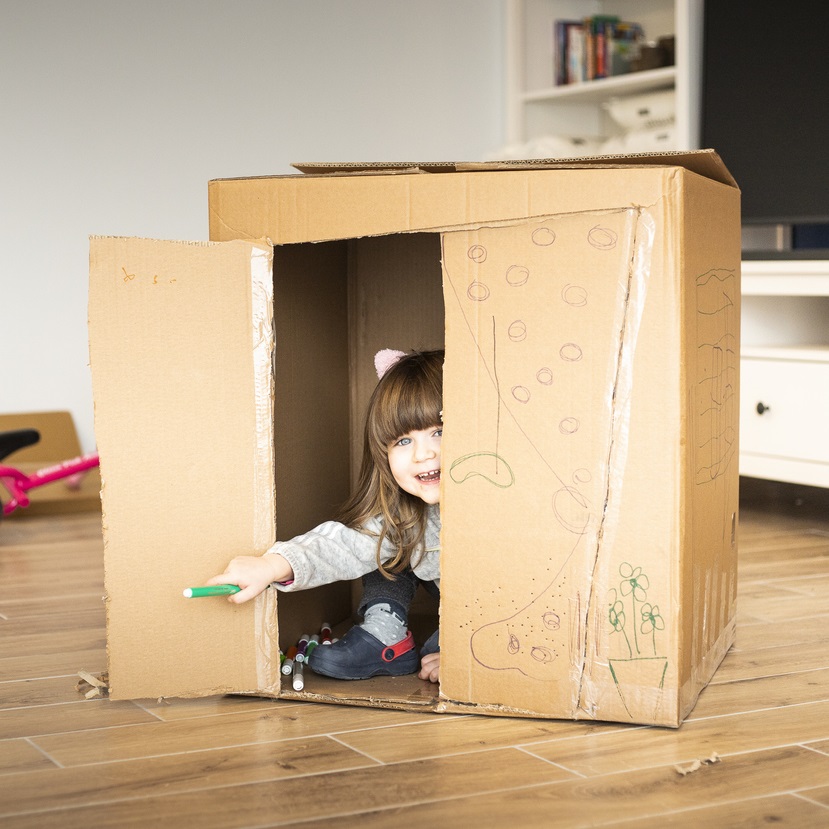 Toddler girl playing inside a big cardboard box
