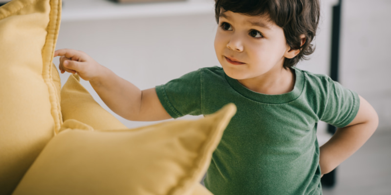 Image of a toddler looking at a pile of cushions built into a fort.