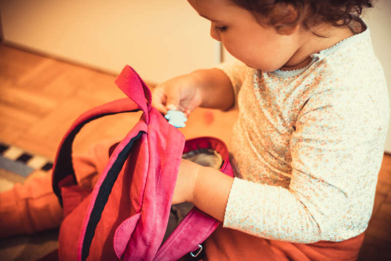 Image of a toddler putting toys in a pink backpack.