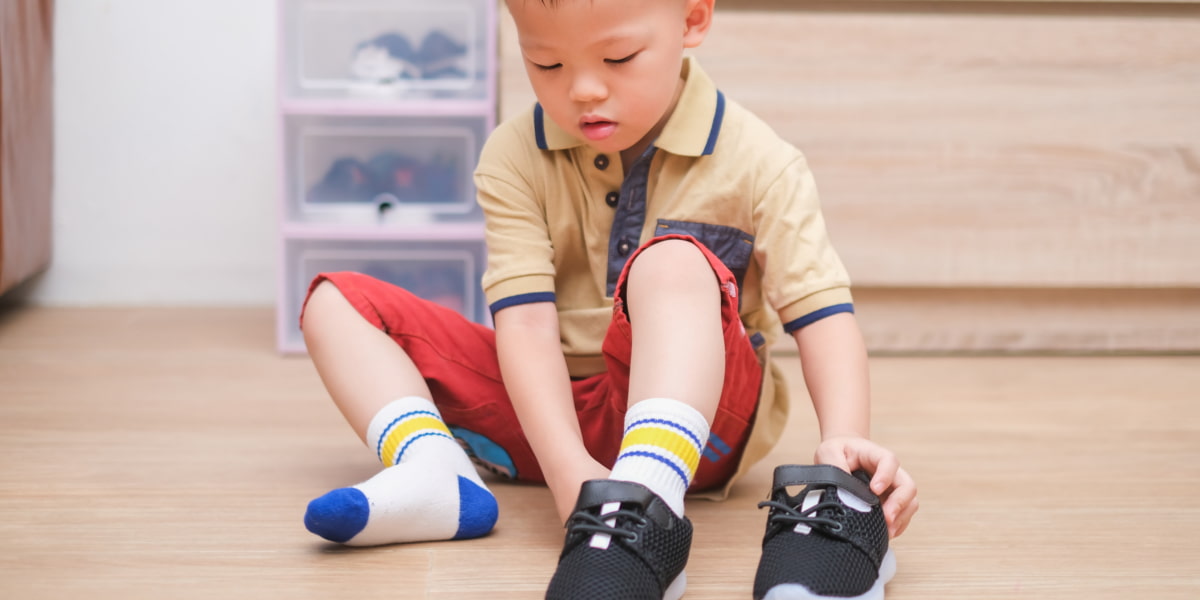 Image of a toddler sitting on the floor putting their shoes on.