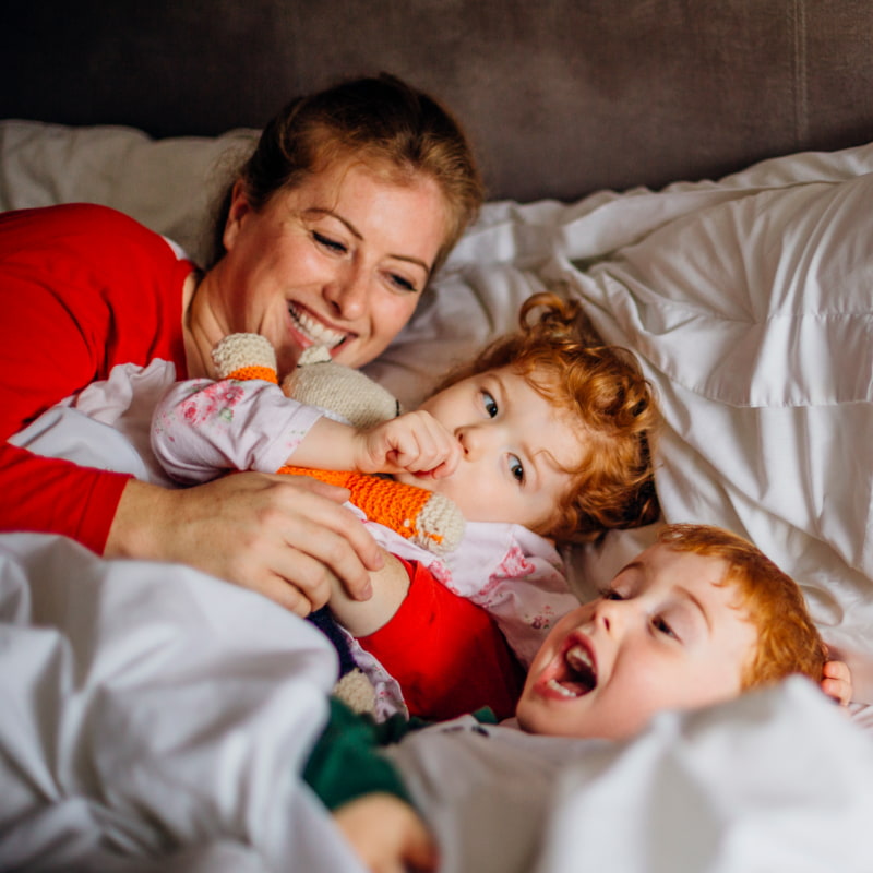 photo of mum and toddlers laughing in bed