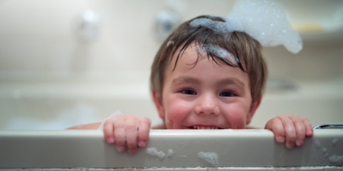 Image of a toddler smiling at the camera with bubbles in their hair.