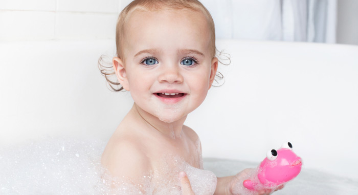 Image of a toddler smiling in a bubble bath, holding a pink toy fish.