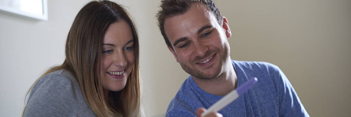 Image of two adults smiling at a pregnancy test.