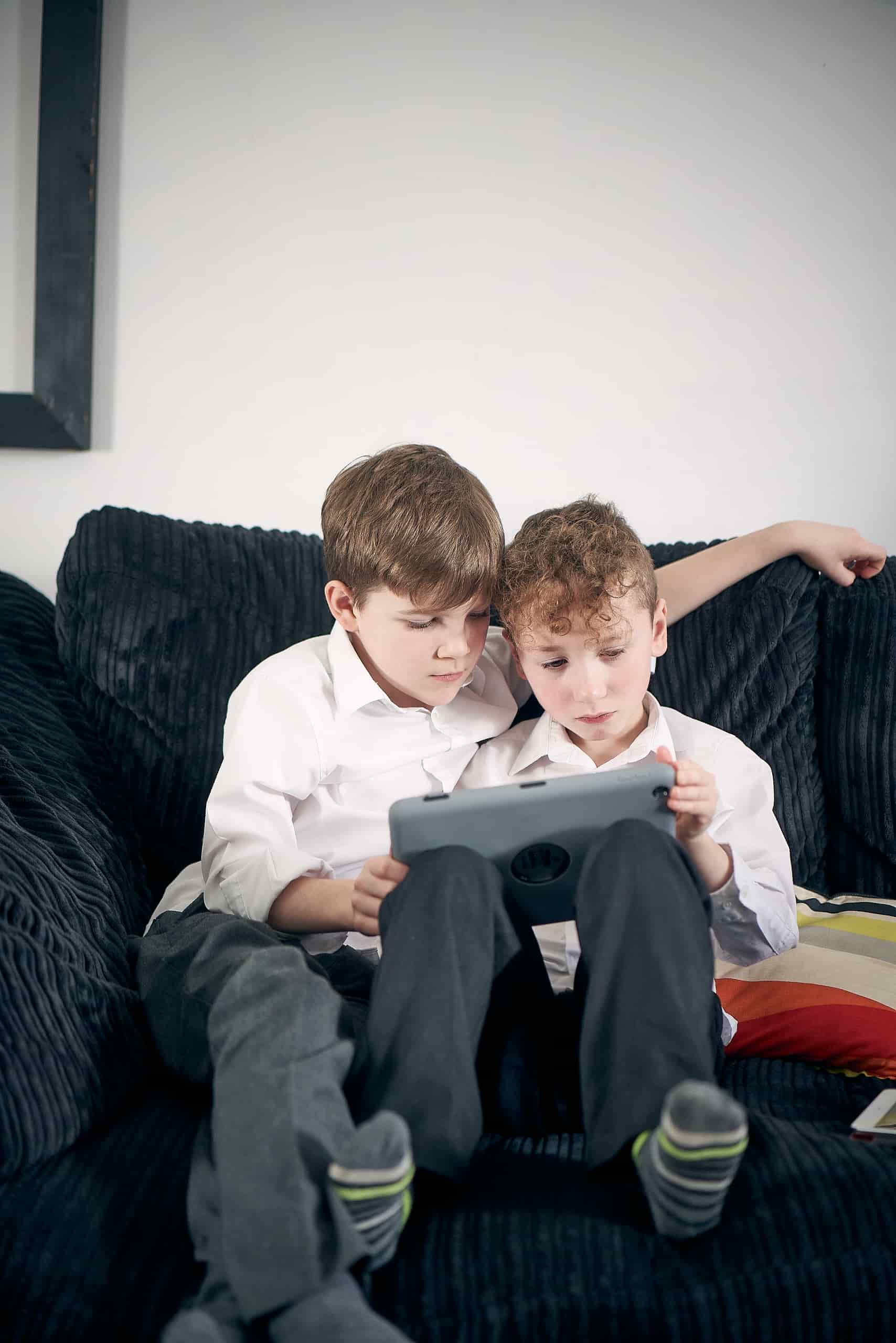 Image of two children sitting next to each other on a sofa looking at an iPad.