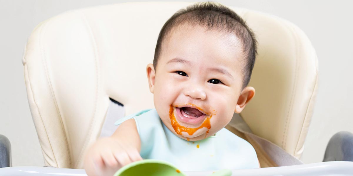 Baby in highchair with tomato soup round their mouth